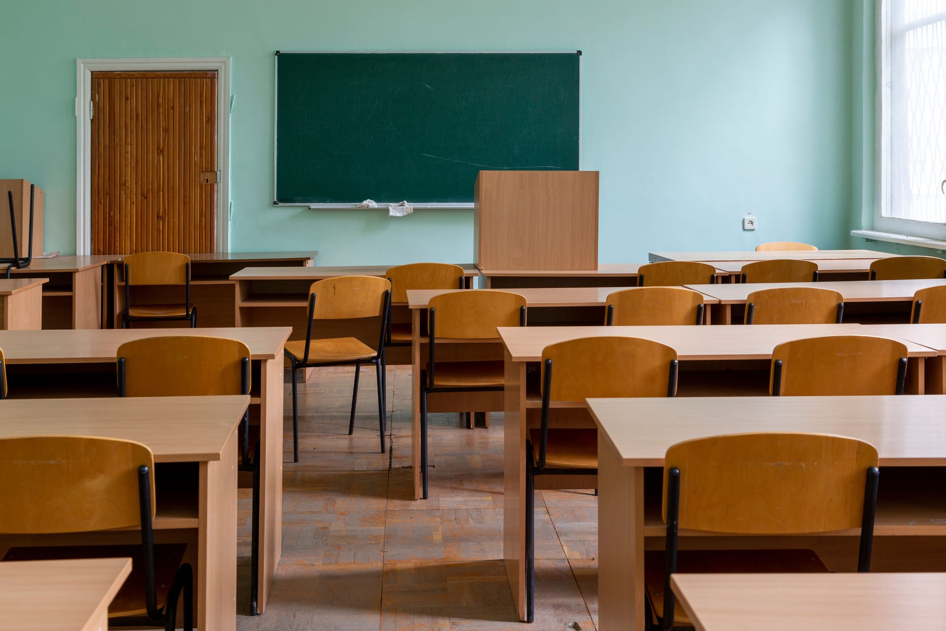 Sala de clases vacía con pizarra y pupitres de madera