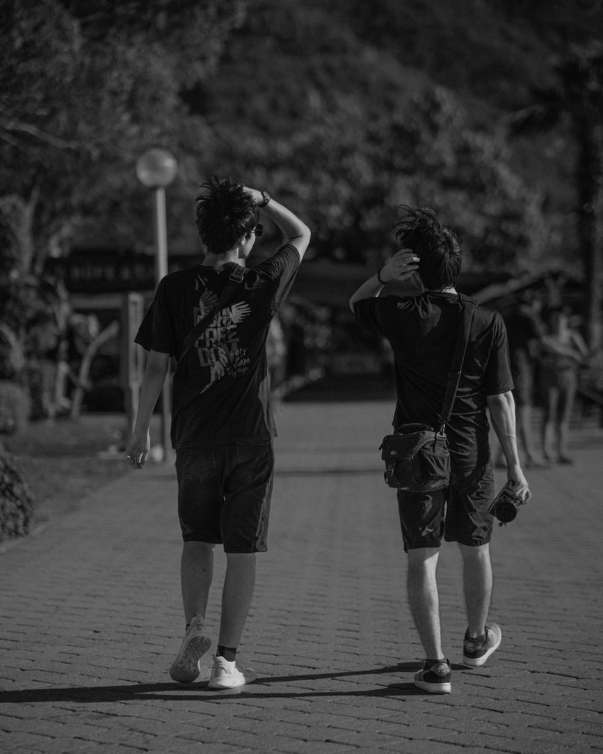 Dos jóvenes caminando de espaldas por una vereda, en blanco y negro